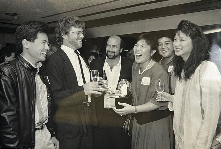 This is an old, black and white photo of Shidler alums eating and drinking and laughing at a networking event.