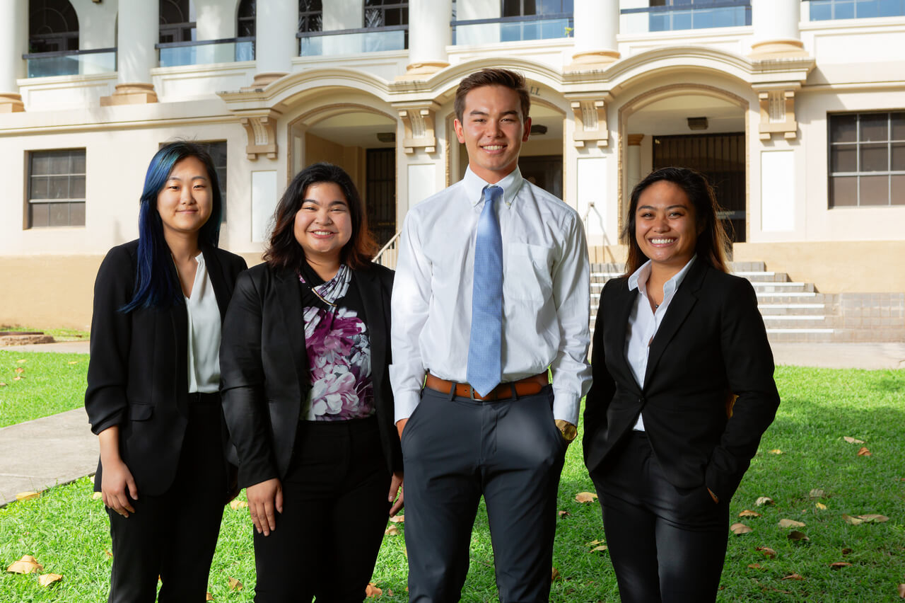 Undergraduate students from The School of Travel Industry Management are dressed formally and standing in front of George Hall.